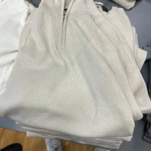 Vit ribbad tröja med dragkedja - Snygg vit tröja med ribbad struktur och dragkedja vid halsen. Perfekt för en stilren och avslappnad look. Passar bra till både jeans och kjol.