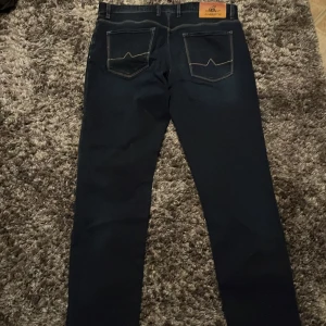 Mörkblå jeans från Alberto - Snygga mörkblå jeans från Alberto med regular fit. Klassisk design med fem fickor och en läderpatch med logotyp på baksidan. Perfekta för en stilren look. W35 L30