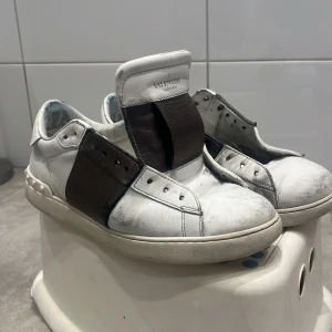 Valentino sneakers i vitt och svart - Snygga Valentino sneakers i vitt med svarta detaljer. Skorna har en stilren design med breda remmar över vristen och en klassisk rund tå. Perfekta för en trendig look. Säljer pågrund av suget av nya dojor.