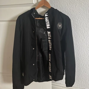 Svart jacka från Philipp Plein - Säljer en svart jacka från Philipp Plein med dragkedja och tryckknappar då den inte kommit till användning. Ny med prislapp. 