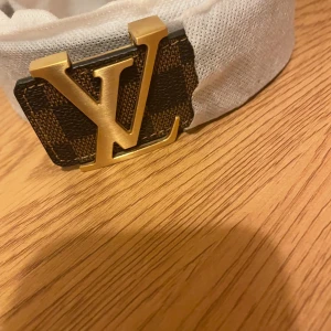 Brunt bälte från Louis Vuitton - Säljer ett brunt bälte från Louis Vuitton med ett klassiskt rutigt mönster och en elegant guldspänne med LV-logotypen. Kommer med originalförpackning och kvitto.