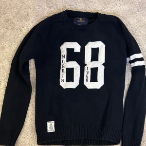 Svart tröja från Morris Gent's - Säljer en svart tröja från Morris Gent's med stort vitt tryck '68' på framsidan och texten 'Morris 1968'. Tröjan har långa ärmar och en ribbad kant vid ärmslut och nederkant. Perfekt för en sportig look!