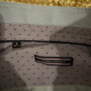 Randig skjorta från Tommy Hilfiger - Snygg och stilren skjorta från Tommy Hilfiger i blå och vit randigt mönster. Skjortan har långa ärmar och knappar framtill. Perfekt för en klassisk men stilig look.