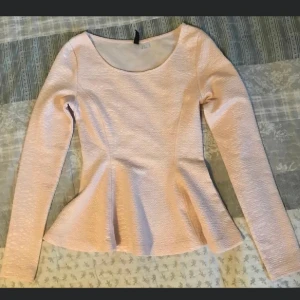 Ljusrosa topp med struktur - Säljer en ljusrosa topp med långärmad design och en fin strukturerad yta. Toppen har en rund halsringning och en lätt utsvängd nederdel som ger en feminin silhuett.