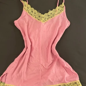 Rosa linne med spetsdetaljer - Säljer ett rosa linne från Gina Tricot med vackra gula spetsdetaljer vid halsringningen och nederkanten. Linnet har smala axelband och en bekväm passform.  Perfekt att ha under våren/sommaren  eller som ett lager under andra plagg.