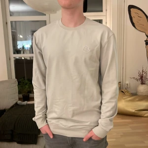 Beige tröja från Moncler - Säljer en stilren beige tröja från Moncler med rund hals och långärmade ärmar. Tröjan har en diskret Moncler-logga på bröstet. 