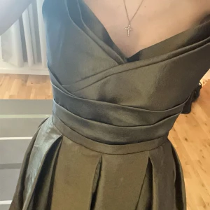 Balklänning  - Elegant grön axelbandslös klänning med veckad kjol och korsad detalj vid bysten. Perfekt för en speciell kväll. Klänningen har en vacker glans och en lång, flödande kjol som ger en sofistikerad look. Skriv så skickar jag mer en gärna en hel bild på klänningen, då Plick klipper bilderna på ett konstigt sätt 😀