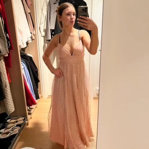 Rosa glittrig långklänning - Säljer en rosa bal/långklänning med glittrande detaljer och smala axelband. Klänningen har en slits och är v-ringad. Perfekt för speciella tillfällen! Använd än fast 2gånger☺️