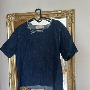 Mörkblå jeanslinnetopp från Our Legacy - Säljer en cool mörkblå jeanslinnetopp från Our Legacy. Toppen har korta ärmar och en rå kant vid halsen och nederkanten för en avslappnad look. Perfekt för en trendig stil!