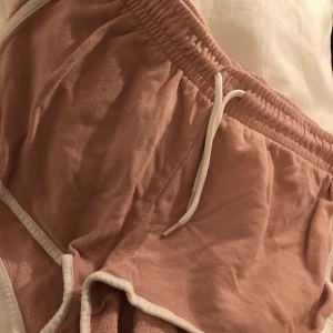 Rosa shorts med snörning - Säljer ett par bekväma rosa shorts med elastisk midja och snörning. Perfekta för en avslappnad dag hemma eller en promenad i solen. De har en mjuk känsla och är lätta att bära.
