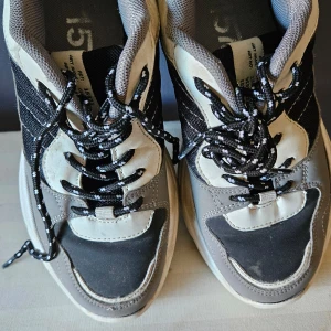 Grå och svarta sneakers med snörning storl.37 från lager 157 - Snygga sneakers i grått och svart med vita detaljer. Skorna har en robust sula och klassisk snörning med svarta och vita skosnören. Perfekta för en avslappnad stil.