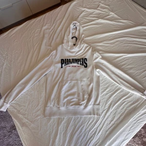 Vit hoodie från Parajumpers - Säljer en vit hoodie från Parajumpers med stor logga på framsidan. Tröjan har en klassisk känguruficka och är tillverkad i mjukt fleecematerial. Perfekt för kyliga dagar med sin bekväma passform och långa ärmar.