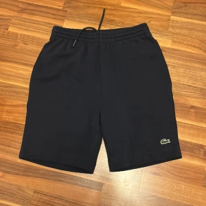 Svarta shorts från Lacoste - Snygga svarta shorts från Lacoste med elastisk midja och snörning. Perfekta för en avslappnad stil. Den klassiska krokodilloggan ger en sportig touch.
