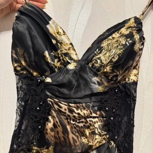 Svart och leopardmönstrad långklänning med spets  - Elegant långklänning med leopardmönster och svarta spetsdetaljer på sidan upptill. Klänningen har smala axelband och en v-ringad design med slits. Storlek 36/38 S/M använd en gång. Pris kan diskuteras och skriv privat för fler bilder 