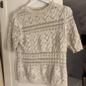 Beige stickad topp från Zara - Säljer en beige stickad topp från Zara med ett vackert spetsmönster. Toppen har korta ärmar och en rund halsringning. Perfekt för en stilren look. 🌟