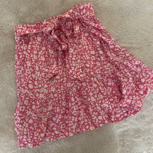 JDY Rosa blommig kjol  - Säljer denna jättesöta rosa blommiga kjolen med knytning från JDY! Den är högmidjad eller medel beroende på hur högt man vill att den ska sitta! Har endast blivit använd en eller två gånger så den har inga defekter 💓💓perfekt till sommaren! 