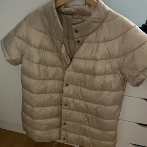 Beige dunjacka från THOM - Säljer en beige dunjacka från THOM med korta ärmar och knappar framtill. Jackan har en stilren design och är perfekt för övergångsperioder. Den är lätt och bekväm att bära.💓