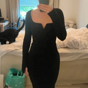 Svart långärmad klänning - Snygg svart klänning med lång ärm och en unik v-ringad design. Perfekt för en elegant look. Klänningen har en tight passform som framhäver figuren. Slutar vid vaderna på mig som är 1,64