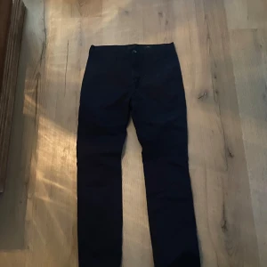 Mörk blå/svarta kostym byxor - Snygga svarta/mörk blå kostym byxor i en blandning av bomull och elastan. Perfekta för en stilren look. Byxorna har en klassisk design med knappar och dragkedja.