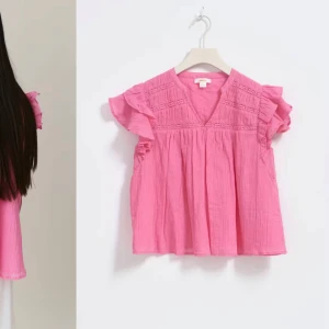 Rosa blus med volangdetaljer - Charmig rosa blus med volangdetaljer på ärmarna och v-ringad hals. Blusen har en luftig passform och är perfekt för varmare dagar. Den har ett fint texturerat mönster upptill som ger extra stil.