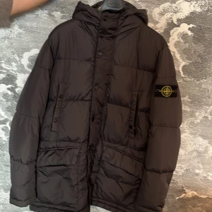 jacka Stone Island - Säljer en svart dunjacka från Stone Island med huva . Jackan har en klassisk design med märkets logga på ärmen. Perfekt för kyliga dagar och håller dig varm och stilren. Jag köpte den på en butik i Göteborg för 6000kr!