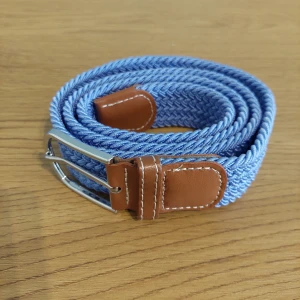 ljus Blått flätat bälte med bruna detaljer - Snyggt blått flätat bälte med bruna läderdetaljer och silverfärgat spänne. Perfekt för att ge en stilren touch till din outfit. Bältet är flexibelt och passar de flesta storlekar.