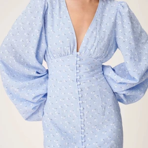 Ljusblå klänning med puffärmar - Säljer en elegant ljusblå klänning med djup v-ringning och puffiga långärmar. Klänningen har knappar framtill. Använd en gång!