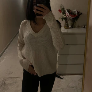 Beige stickad tröja med v-ringning - Säljer en mysig beige/vit stickad tröja med v-ringning. Tröjan har långa ärmar och en öppen ryggdetalj som ger en extra touch. Perfekt för kyligare dagar och lätt att matcha med olika outfits.