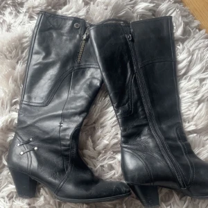 Svarta stövlar med dragkedja - Snygga svarta stövlar i skinn med dragkedja på sidan och dekorativa nitar. De har en låg klack och en stilren design som passar perfekt för höst och vinter.