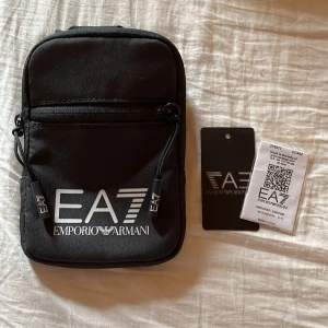 Svart axelväska från Emporio Armani - En snygg trendig axelväska från Armani. Väskan är använd endast någon gång säljer nu den för att jag inte har något behöva av en väska. Den är köpt i Italien. Säljer nu den för ett väldigt bra pris. 400kr