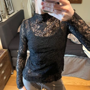 Svart spetsblus från Stockh LM Studio - Säljer en elegant svart spetsblus från Stockh LM Studio. Blusen har långa ärmar och en hög hals, perfekt för en stilren look. Den är tillverkad i ett vackert spetsmaterial som ger en sofistikerad touch.