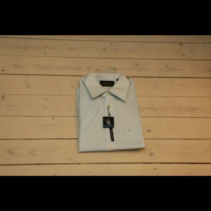 Ljusblå skjorta från Greggio - Snygg ljusblå skjorta från Greggio med klassisk krage och knappar framtill. Perfekt för en stilren look. Skjortan har en liten broderad logga på bröstet.