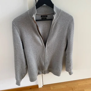 Grå kofta från Massimo Dutti - Snygg grå kofta från Massimo Dutti i en mjuk bomulls- och kashmirblandning. Den har en dragkedja framtill och en stilren design som passar perfekt för både vardag och mer uppklädda tillfällen. Skriv vid frågor! 