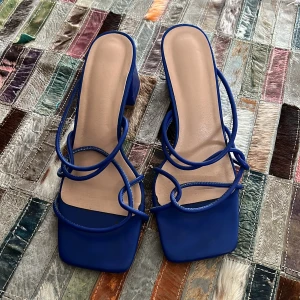 Blå sandaler med klack - Snygga blå sandaler med fyrkantig tå och klack. De har tunna remmar som korsar över foten för en elegant look. Perfekta för att lyfta vilken outfit som helst.