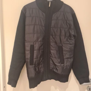 Svart cardigan  - Snygg svart cardigan jacka med dun på framsidan och stickade ärmar och baksida. Jackan har en dragkedja framtill och ribbade muddar. Knappt använd, passade inte mig Storlek xs