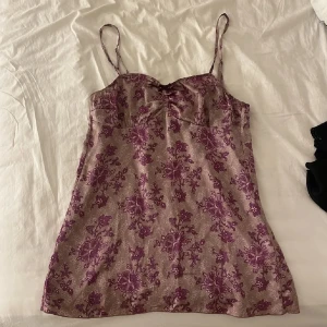 Blommig topp med smala axelband - Säljer en söt klänning med smala axelband och ett blommigt mönster i lila nyanser. Perfekt för varma dagar med sin lätta och luftiga design.