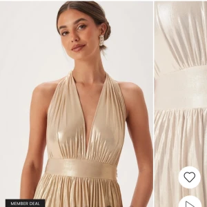 Champagnefärgad långklänning med djup V-ringning - Säljer min gamla balklänning från bubbelroom, använd 1 gång, inga slitagetecken, skriv privat för egna bilder. Köparen står för frakt💕                                                        Elegant champagnefärgad långklänning med djup V-ringning och halterneck-design. Klänningen har en glansig finish och ett brett band i midjan som ger en smickrande silhuett. Perfekt för en glamorös kväll.