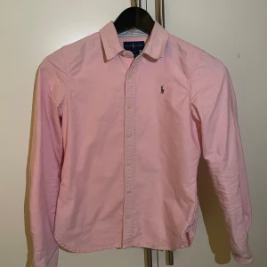 Ralph lauren skjorta - Rosa skjorta från Ralph lauren .  Väldigt bra skick, nästan som ny, 9/10 skick. Använt några gånger. Blivit för liten. Storlek 12 som är 152 cm men passar även 158.