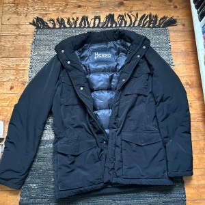 Svart dunjacka från Herno - Säljer en svart dunjacka från Herno, perfekt för kalla dagar. Jackan är vattentät och har en stilren design med dragkedja och knappar. Tillverkad i Italien med högkvalitativt dunfoder för extra värme. Ett måste för vintern!                                            Cond: 8/10