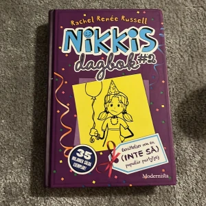 Nikkis dagbok #2 - Säljer 'Nikkis dagbok #2' av Rachel Renée Russell. Boken har en lila omslag med en tecknad bild av en flicka med en partyhatt. Den är en del av en populär serie och innehåller humoristiska berättelser om en (inte så) populär partytjej. Perfekt för ungdomar som gillar dagboksstil och roliga illustrationer.