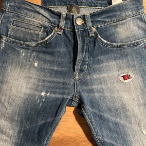Dondup jeans  - Snygga blå jeans med slitningar och en cool, distressed look. De har en slim passform och är perfekta för en avslappnad stil. Jeansen har klassiska fem fickor och en knappgylf. Skicket är som nya! Han på bilden väger 67 och är runt 178 cm lång!