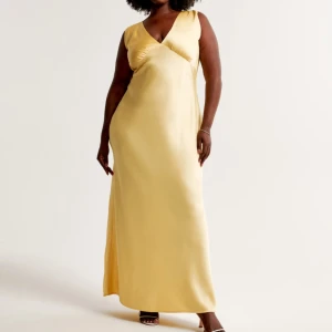 Gul långklänning med öppen rygg - Elegant gul långklänning i satin med v-ringad framsida och öppen rygg. Klänningen har en vacker drapering baktill och knytband i nacken. En perfekt klänning som hade passat perfekt till balen, men tyvärr va den lite för liten för mig. Helt ny med prislapp kvar 