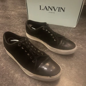 Lanvin - Snygga svarta sneakers från Lanvin med en stilren design. Skorna har en blank yta och klassisk snörning. Perfekta för en stilmedveten look. Uk 10 Storlek 44 Pris 1300