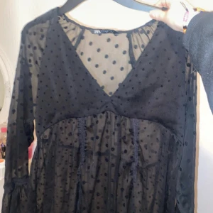 Svart prickig blus från Zara - Snygg svart blus från Zara med prickigt mönster och v-ringning. Blusen har långa ärmar och är tillverkad i ett transparent material som ger en elegant look. Perfekt för att lägga till en touch av stil till din garderob.