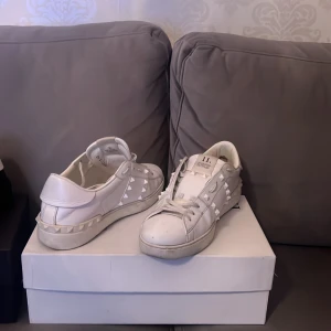 Valentinos  - Snygga vita sneakers med nitar runtom för en edgy look. Skorna har snörning och en klassisk design som passar perfekt till olika stilar. Perfekta för dig som vill ha något unikt och stilrent.