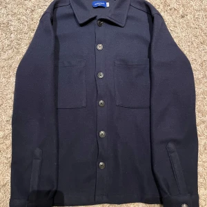 Mörkblå overshirt från Jack&Jones - Snygg mörkblå overshirt från Jack&Jones med knappar framtill och två bröstfickor. Perfekt för lager-på-lager-stil. Passar till de flesta stilar och outfits!