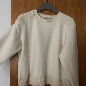 Vit stickad tröja från Zara - Säljer en stilren vit stickad tröja från Zara. Tröjan har långa ärmar och ribbade detaljer vid axlar och nederkant. Snygg och enkel att matcha med olika outfits.