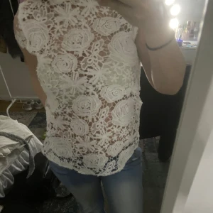 Vit spetsblus - Säljer en elegant vit spetsblus med blommigt mönster. Blusen är kortärmad. Perfekt för en stilren look. Använt 2 gånger.