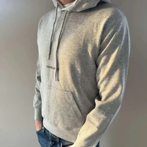 Grå hoodie från Saint Laurent - Snygg grå hoodie från Saint Laurent med justerbar huva och känguruficka. Perfekt för en avslappnad stil. Den har en diskret logga på bröstet och långa ärmar med ribbade muddar. Är 177 och väger 65 kg