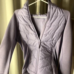 Ljuslila quiltad jacka - Säljer en ljuslila quiltad jacka med dragkedja. Jackan har en figurnära passform och långa ärmar. Perfekt för kyligare dagar med sin stilrena design och bekväma material.